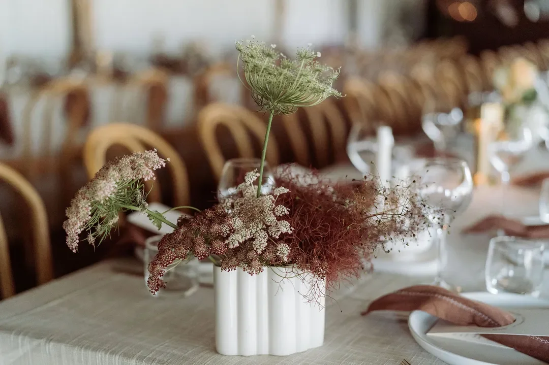 Minimalist white vase with queen anne’s lace and smoke bush styled on a banquet table at the wedding reception.