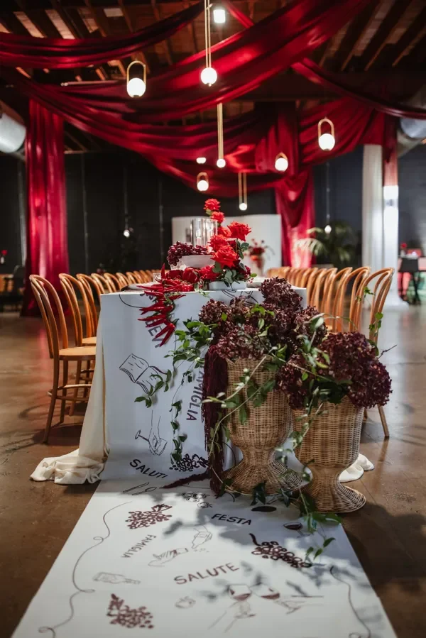 Long banquet table with red roses, glass candle cylinders and Italian-inspired table décor for an event in Brisbane.