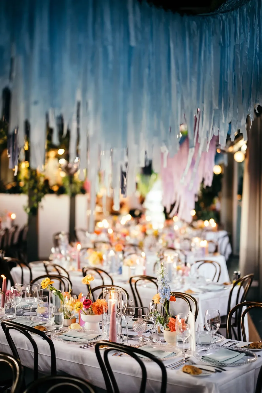 Wedding reception tables styled with colourful flowers, candles, and hanging blue streamers for Sarah and Marshall’s celebration.