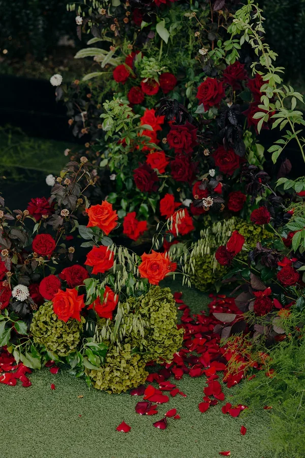 Red rose petals and textured floral arrangements lining the wedding ceremony aisle