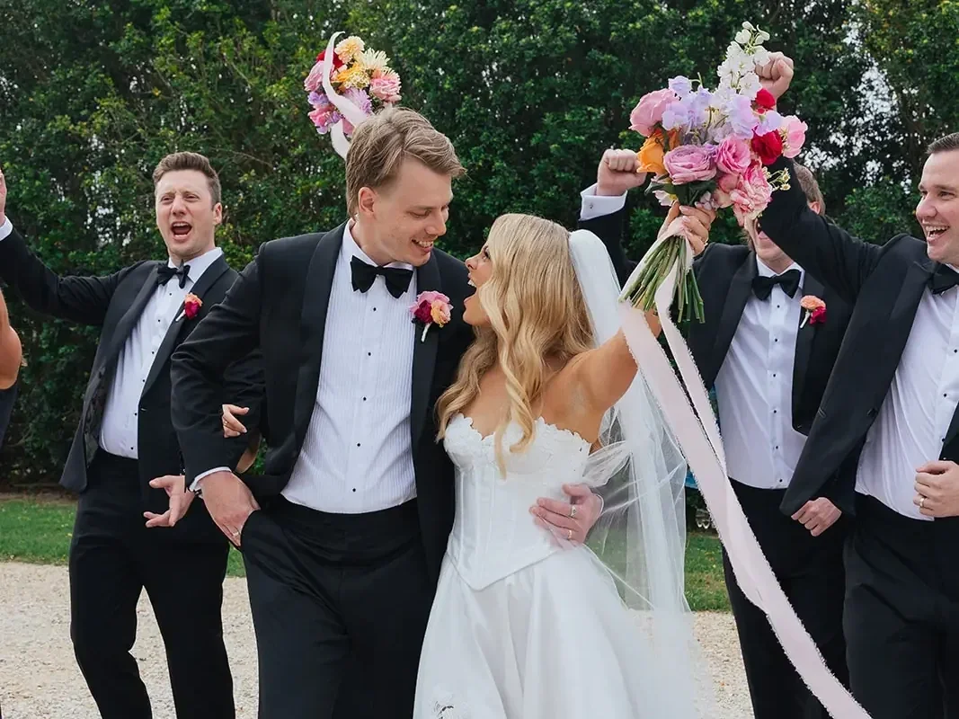 Bride and groom celebrating with their wedding party, holding bright pastel bouquets with pink, peach and lavender flowers at a Brisbane wedding.