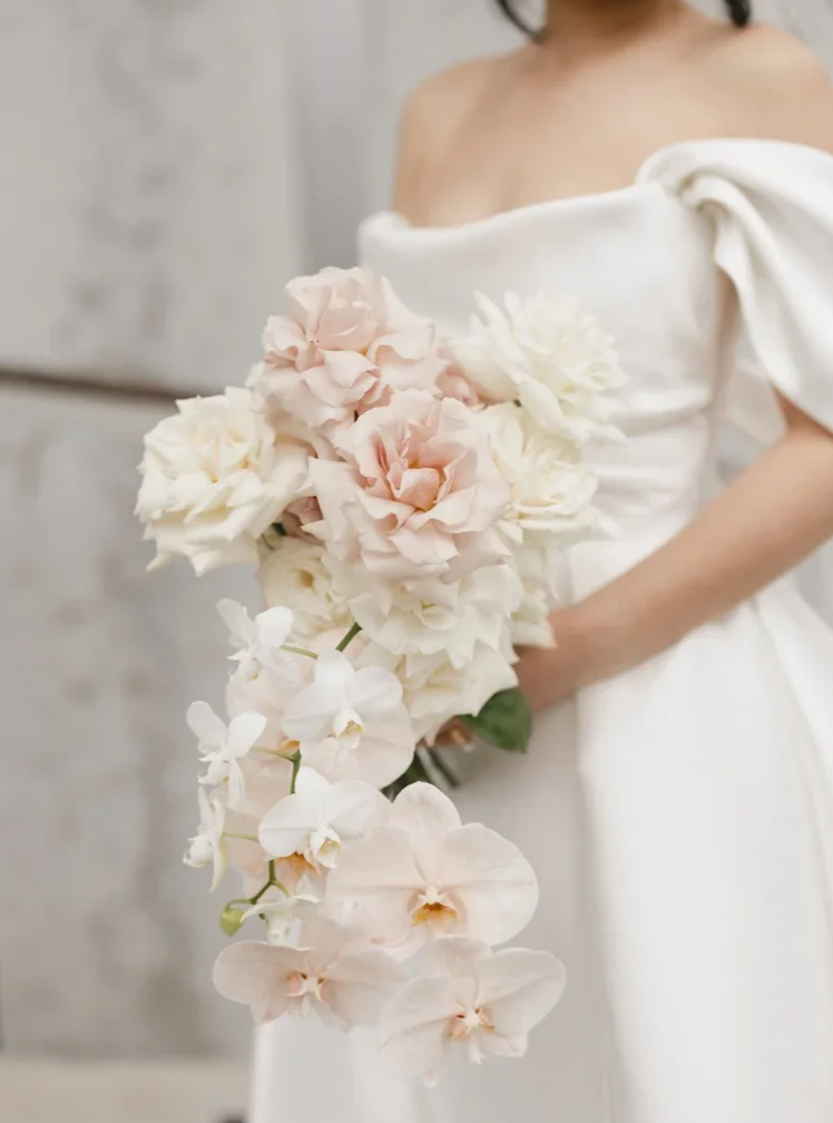 Bride in modern silk dress hold bouquet of white orchids while holding champagne glass