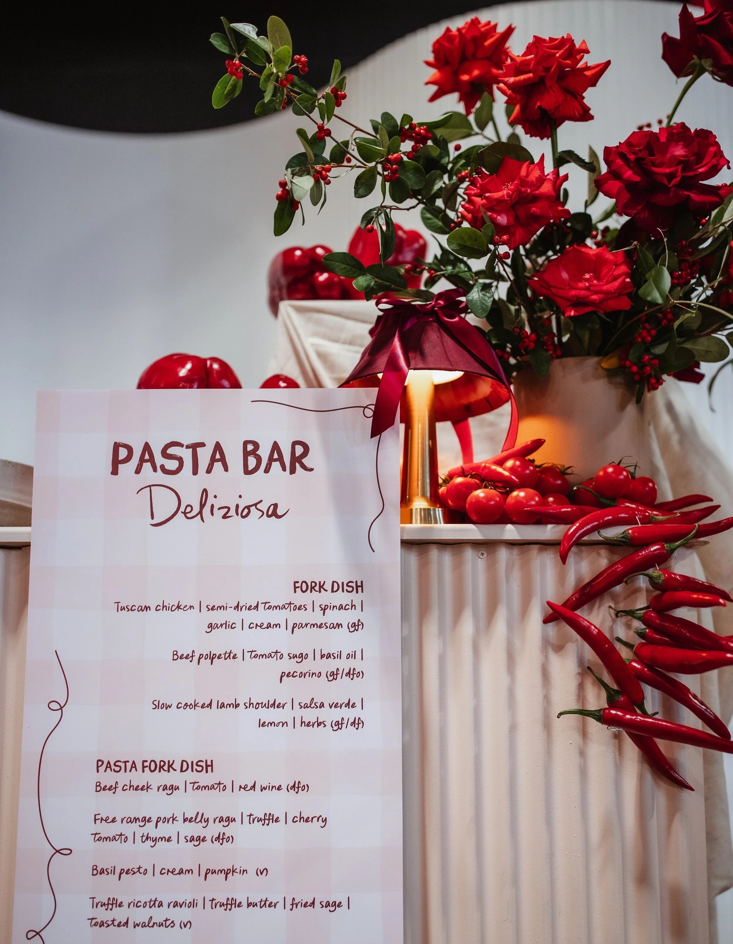 Menu of pasta bar with red rose floral arrangement and cascading chillies and tomatoes