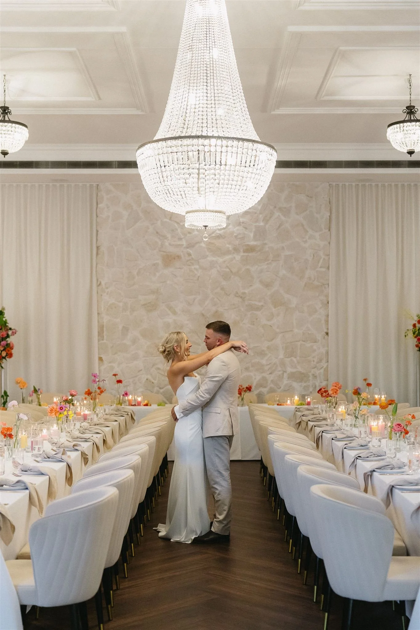 newlywed couple embracing in reception space decorated with wedding flowers