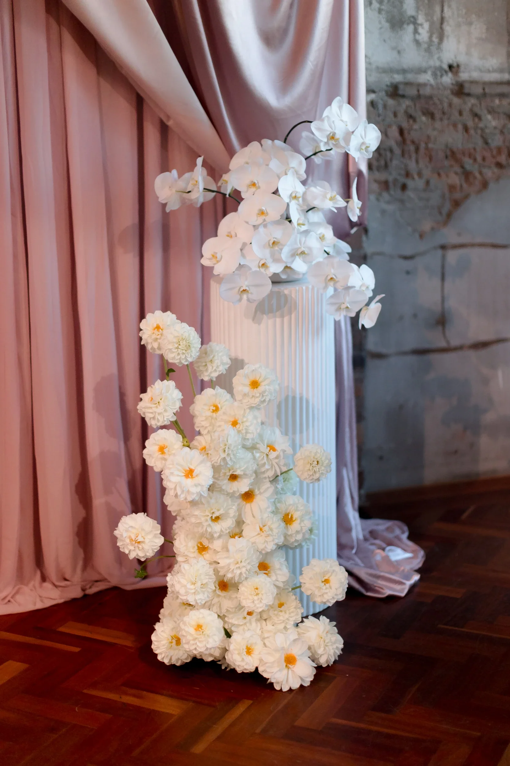 White orchid and bloom floral column beside blush silk drapery at a Fortitude Valley wedding ceremony