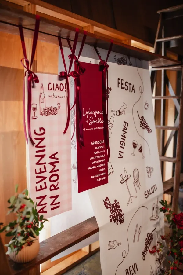 Italian illustrated signage display with red ribbons and event sponsor panels styled by a Brisbane florist.