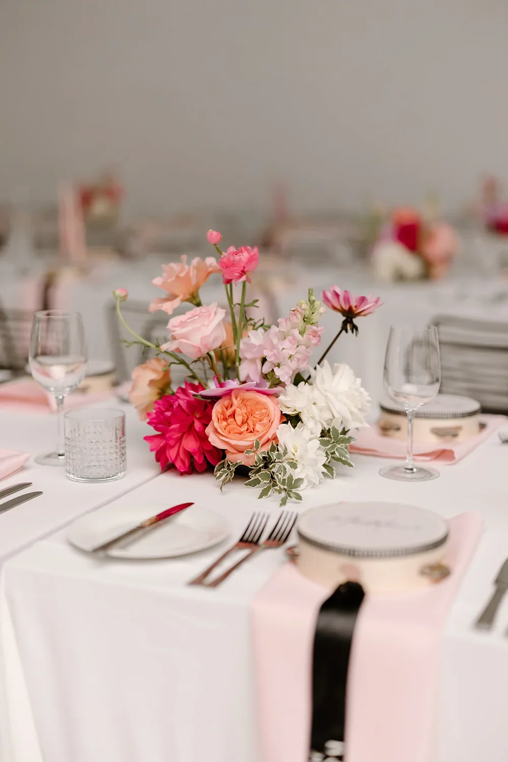 Wedding reception table setting featuring pastel florals, glassware, and blush napkins on a white-draped table.