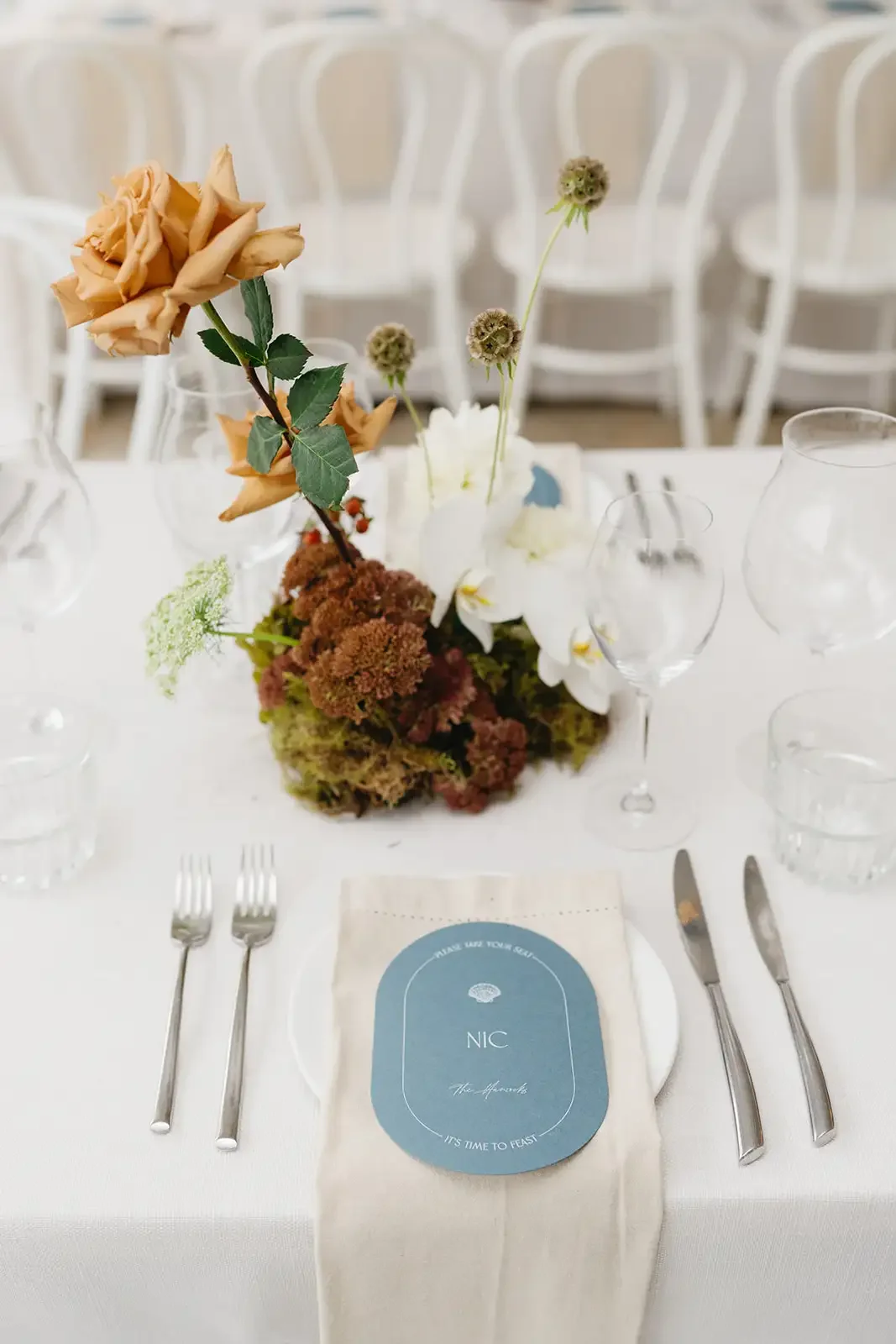 Reception table styling with tan roses, white orchids, moss and coastal-inspired place cards.