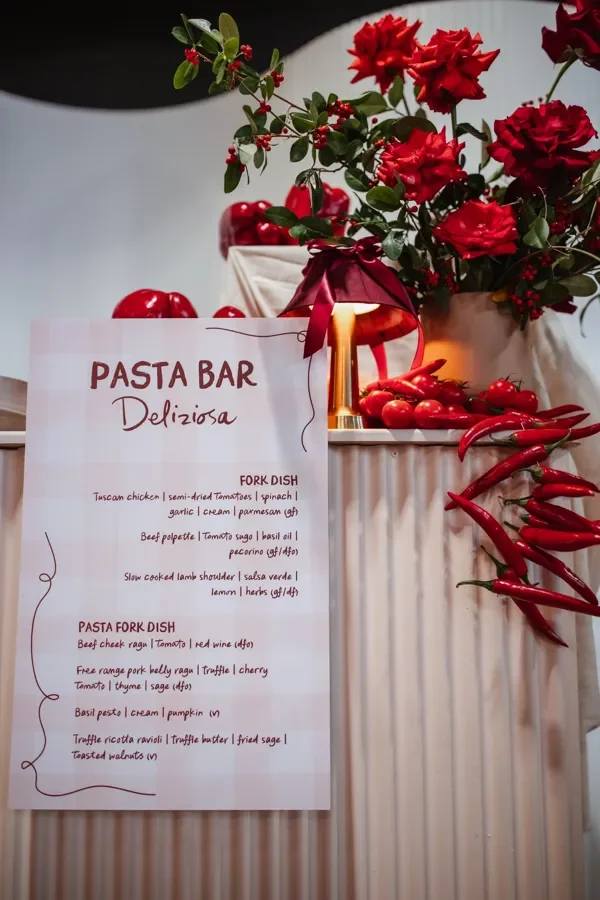 Pasta bar station styled with red roses, fresh produce and handwritten Italian menu signage at a Brisbane event.