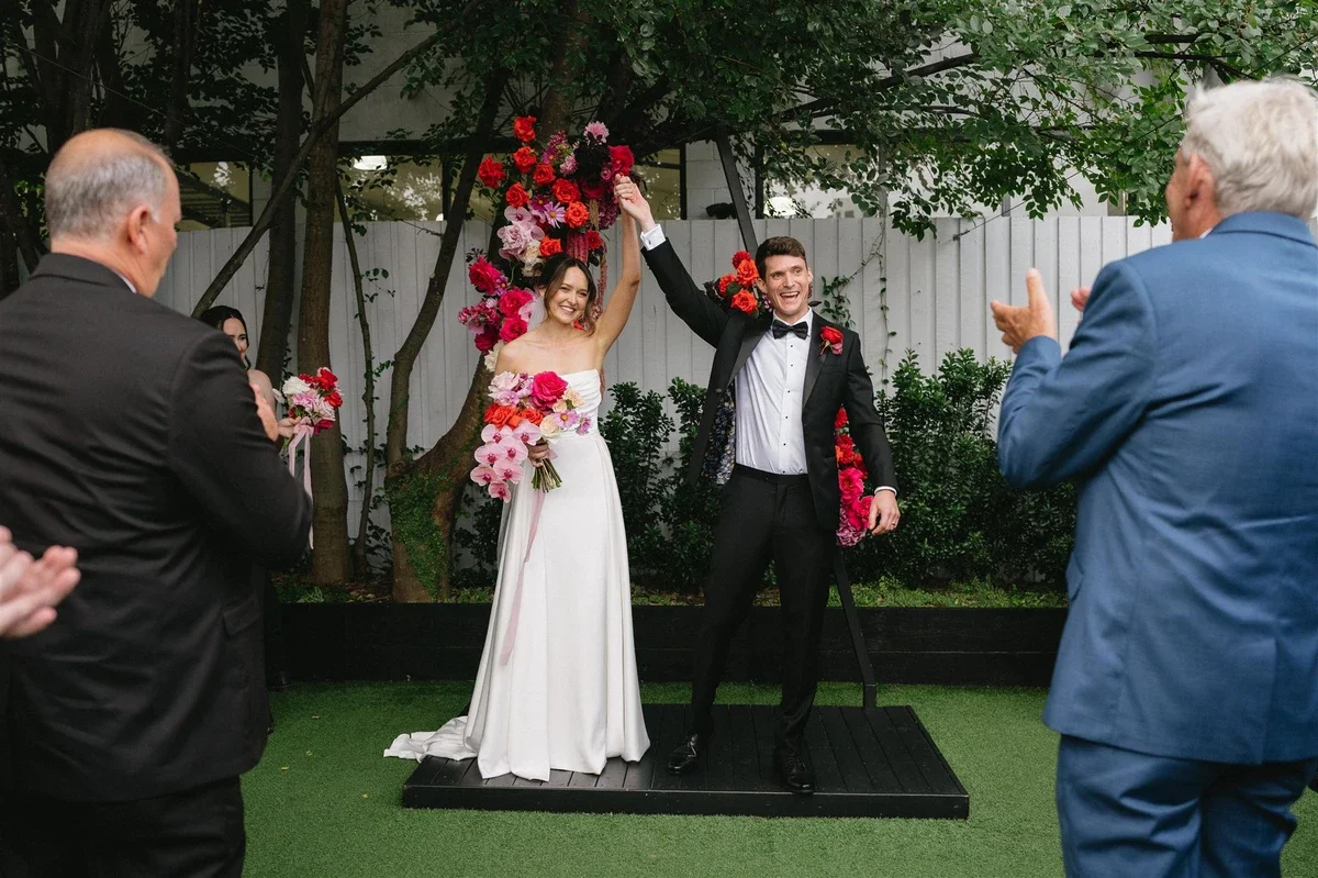 Bride and groom celebrating as they walk down the aisle with bold red, pink and peach florals.