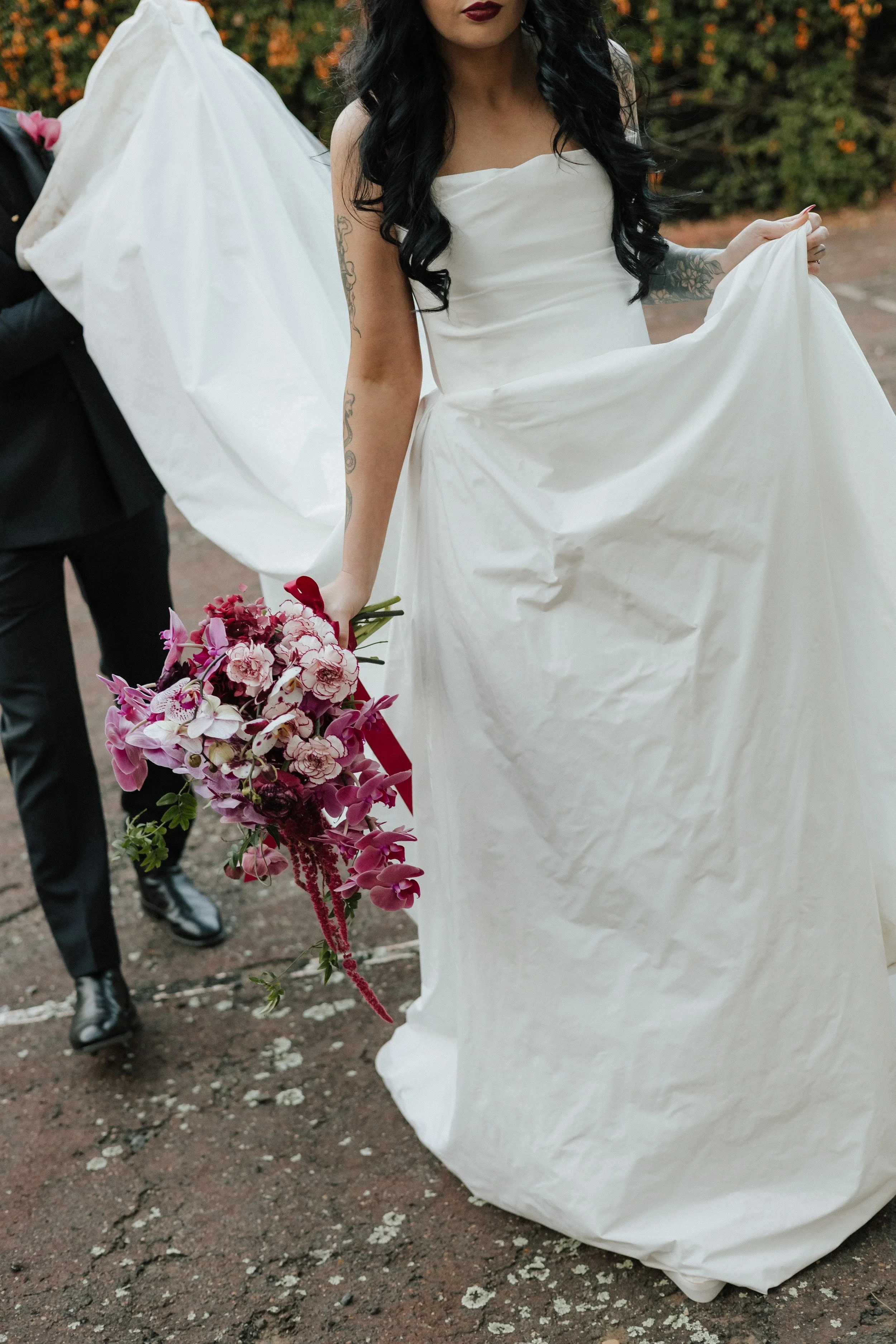 Bride lifting her white gown with a pink orchid and deep red bouquet in hand