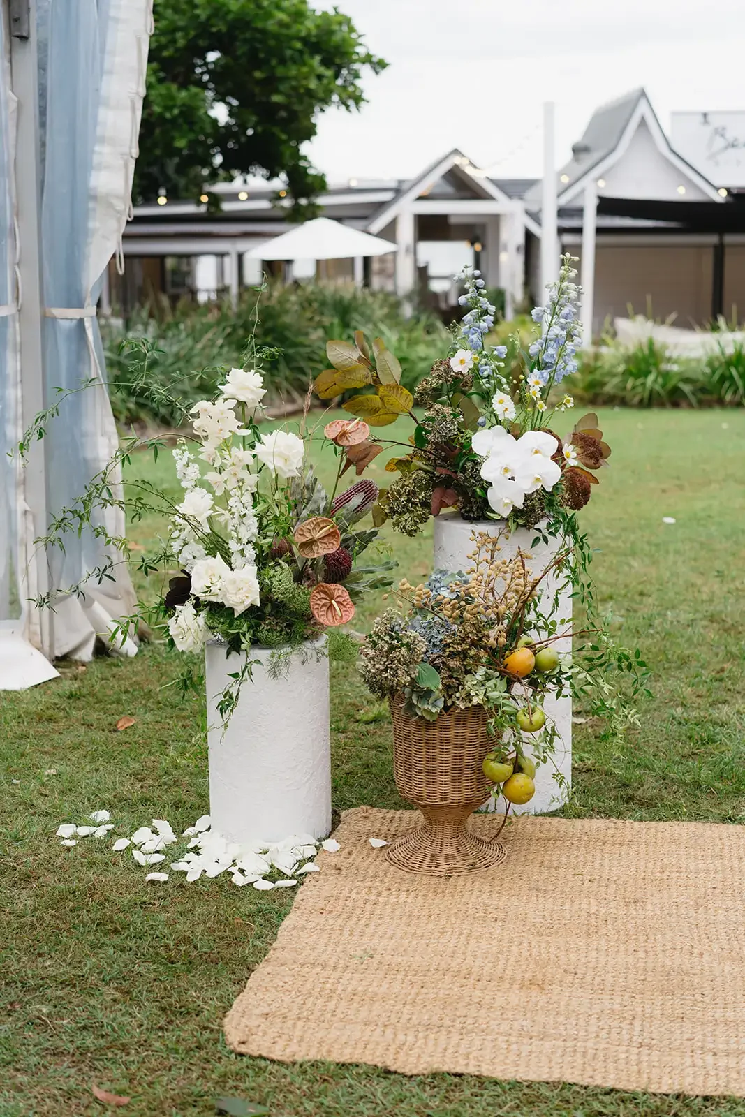 Ceremony flower arrangements in earthy tones with orchids and foliage on white plinths.
