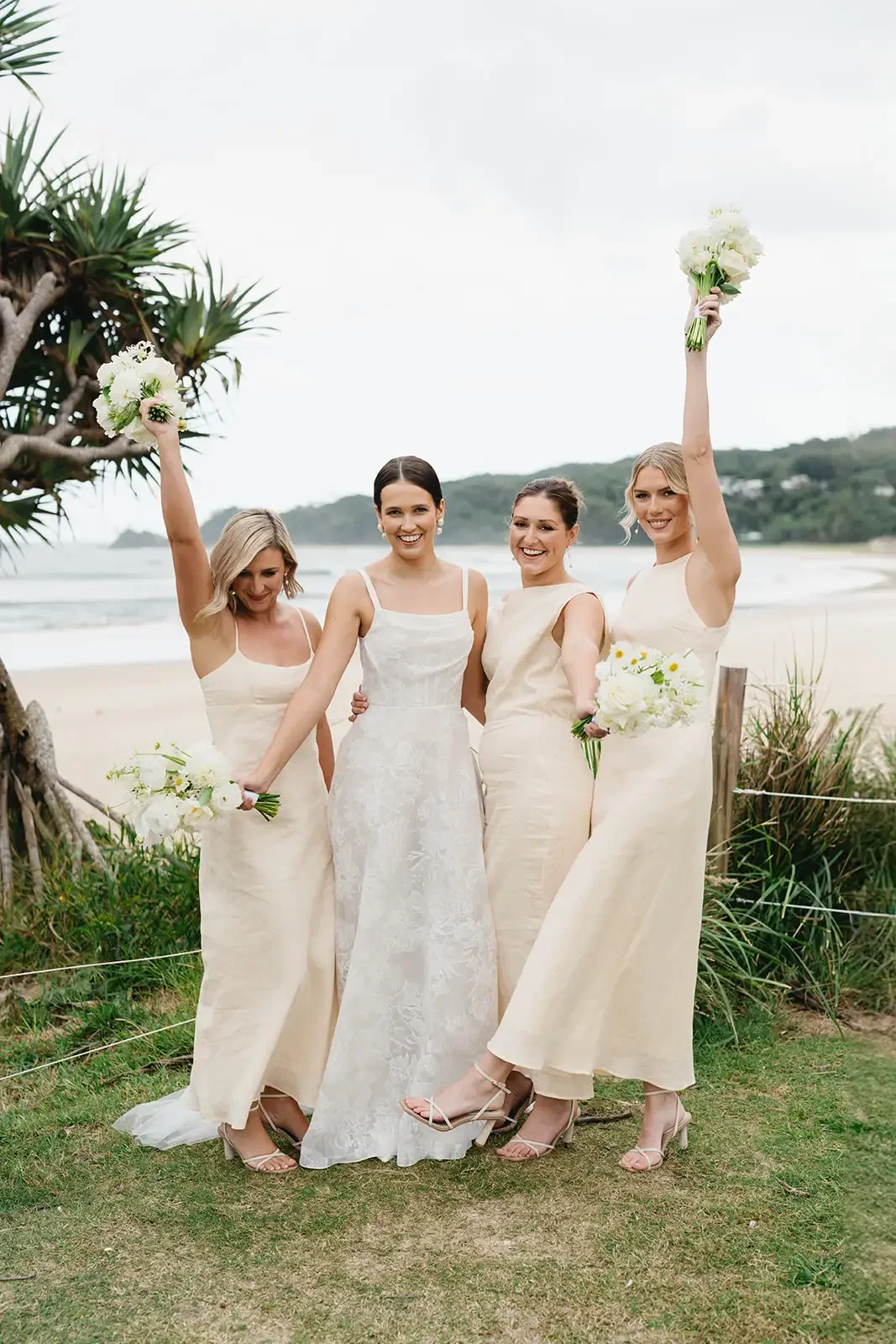 Bride and bridesmaids posing together with white bouquets at a Byron Bay beachside wedding.