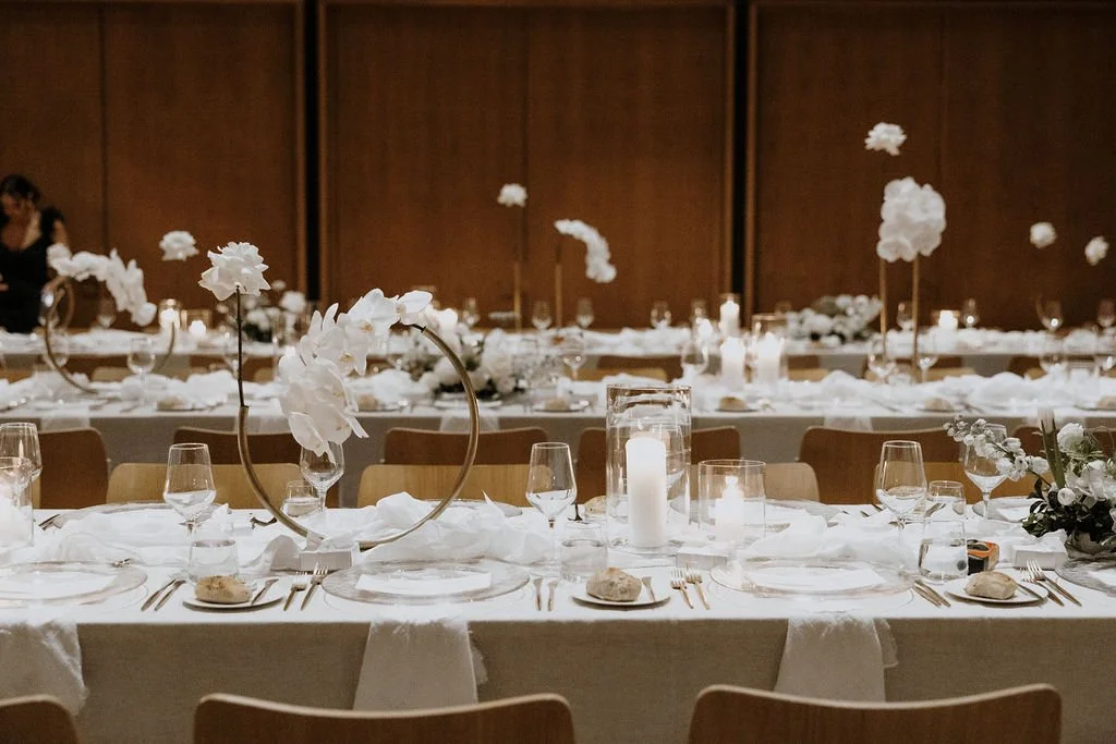 Minimalist white orchid centrepieces on gold stands along candlelit reception tables.