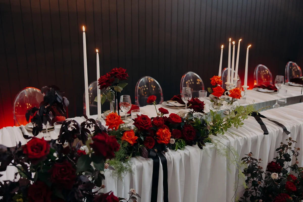 Close up of red rose floral arrangement with white layered table linen, mirror runners and candlelight.