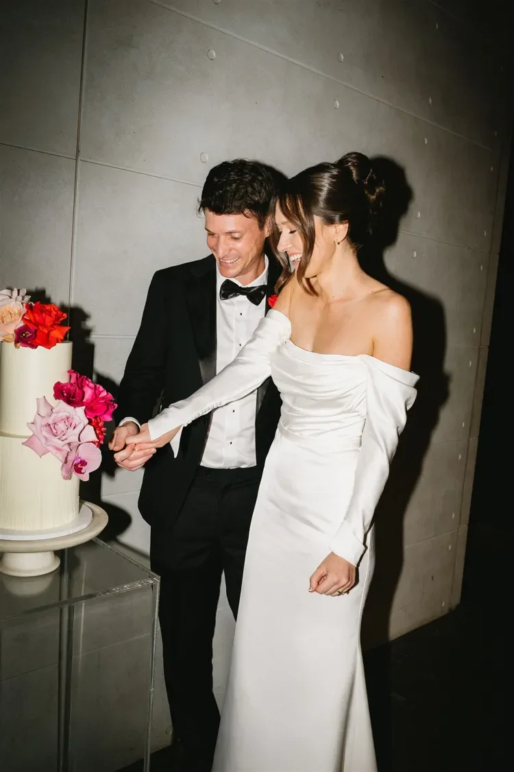 Bride and groom smiling as they cut their colourful floral wedding cake together during the reception.