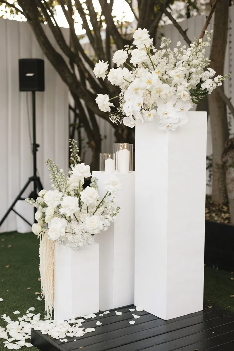 Side view of white floral pillars with cascading orchids, roses, and candles arranged for a modern outdoor ceremony.
