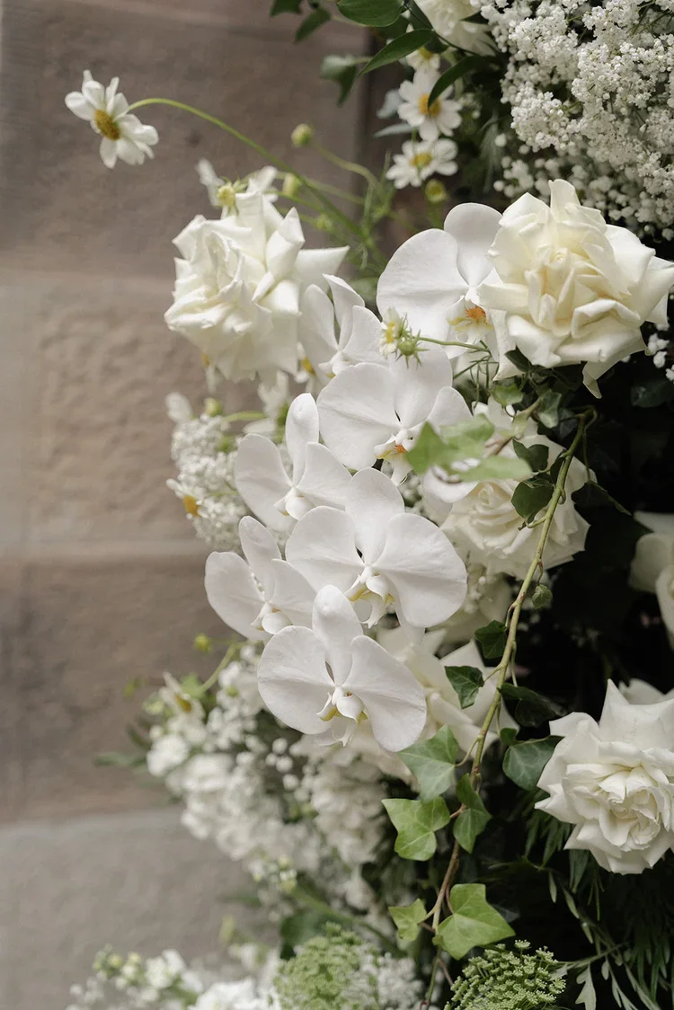 Close-up of white orchids and roses in the ceremony floral installation, styled with greenery and delicate filler blooms.
