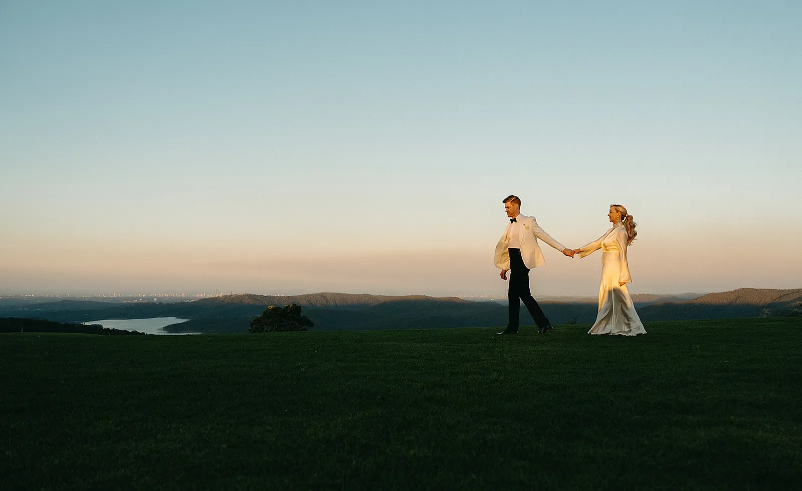 Bride and groom holding hands on a hilltop at sunset with expansive Scenic Rim landscape views behind them.