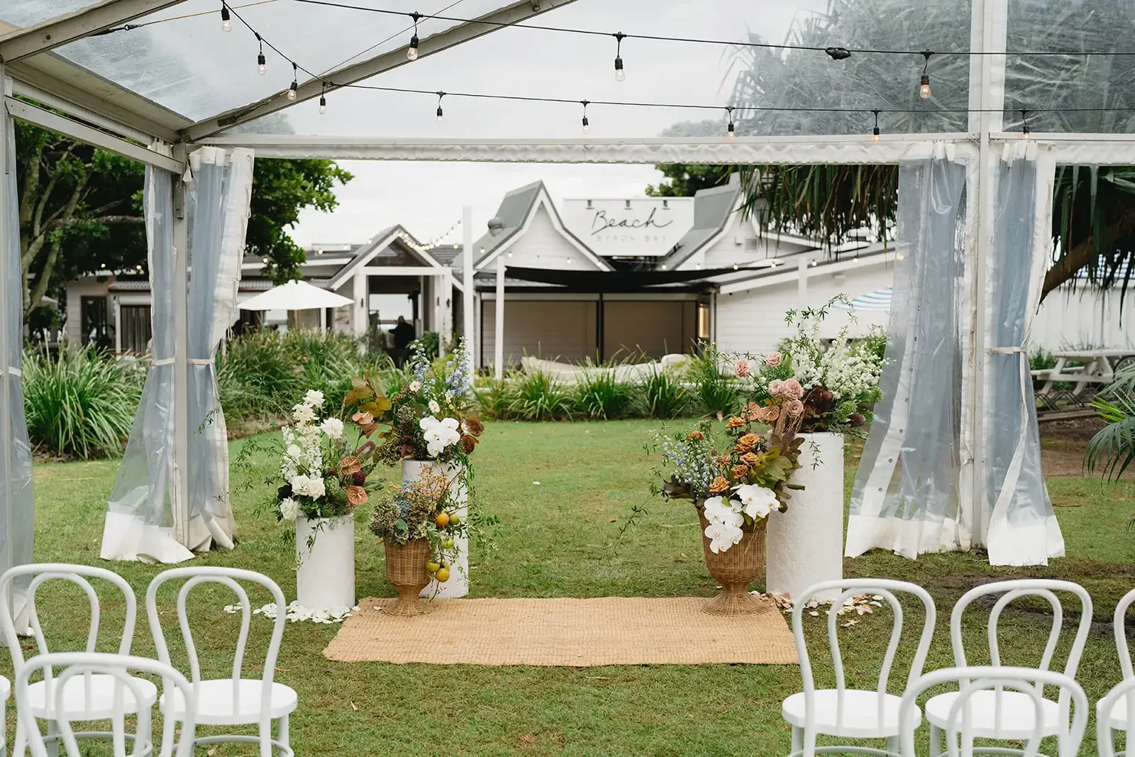 Byron Bay outdoor ceremony setup with coastal-inspired wedding flowers and white chairs.