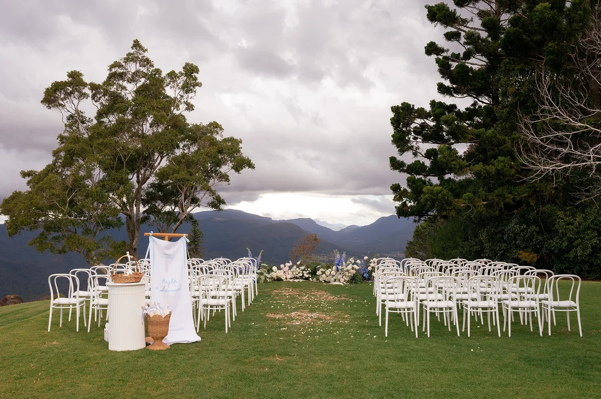 Outdoor ceremony setup with white chairs and lush blue and white florals overlooking panoramic mountain views at a Scenic Rim wedding.
