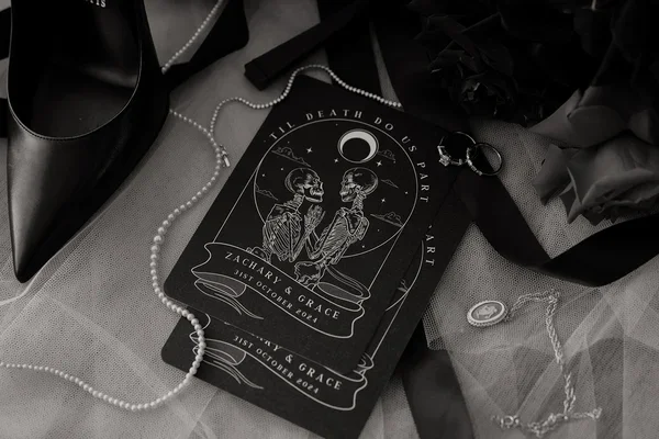 Flatlay of gothic-inspired wedding invitations with skeleton illustrations, pearls and black accents.