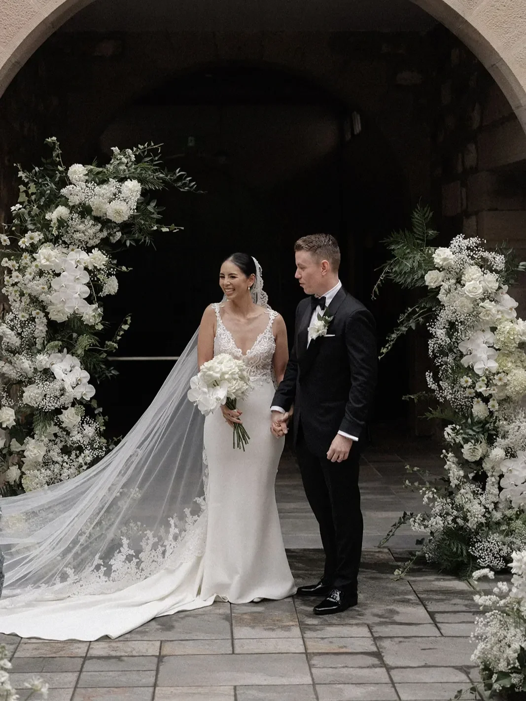 newlywed couple standing beneath a floral arch at Brisbane Old Government House during wedding ceremony