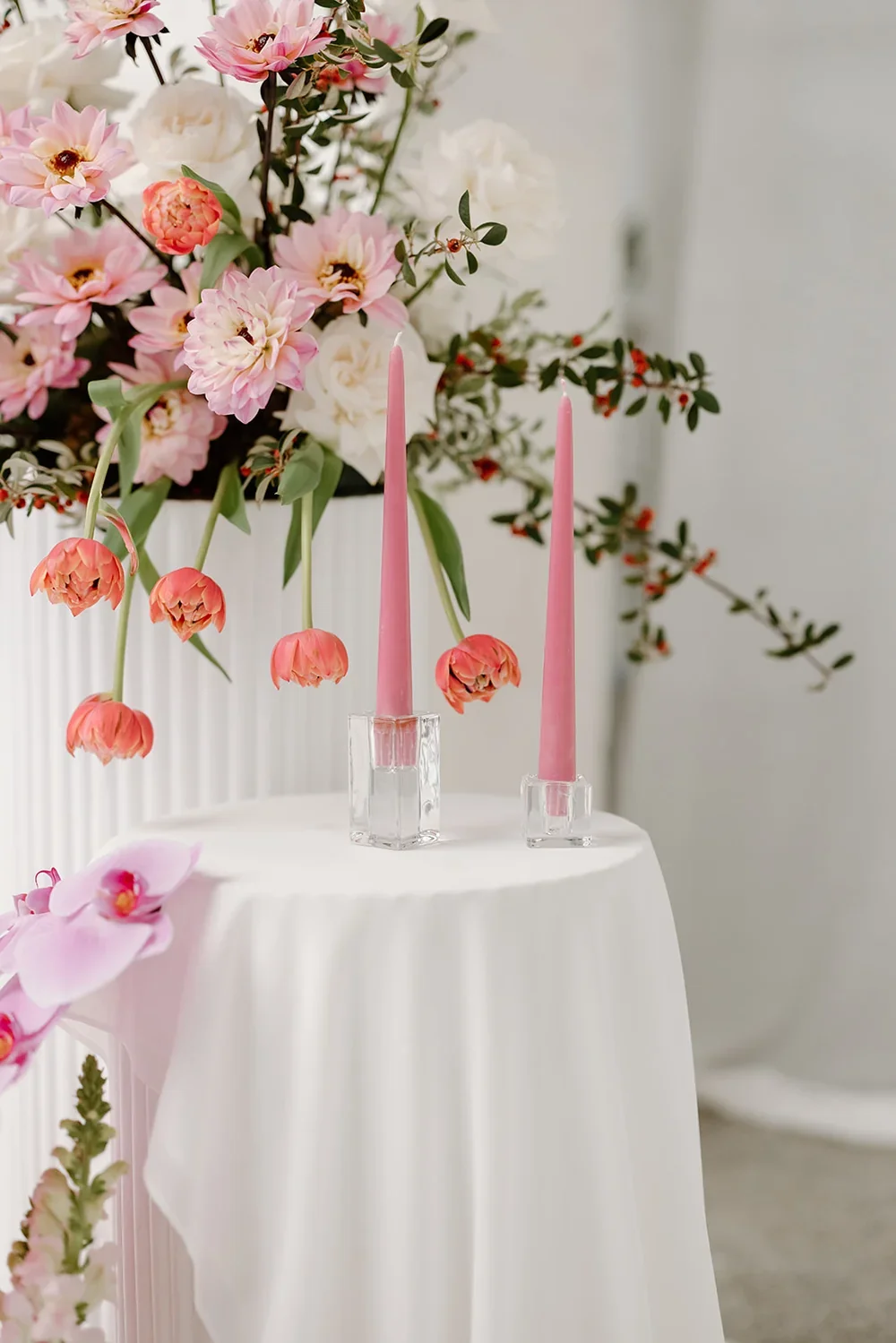 Close up of two pink taper candles with cascading tulips in background on white fabric draped plinth