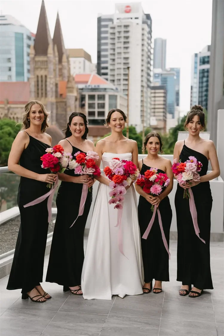 Bride and bridesmaids laughing and walking together outside The Refinery, holding vibrant multi-coloured bouquets.