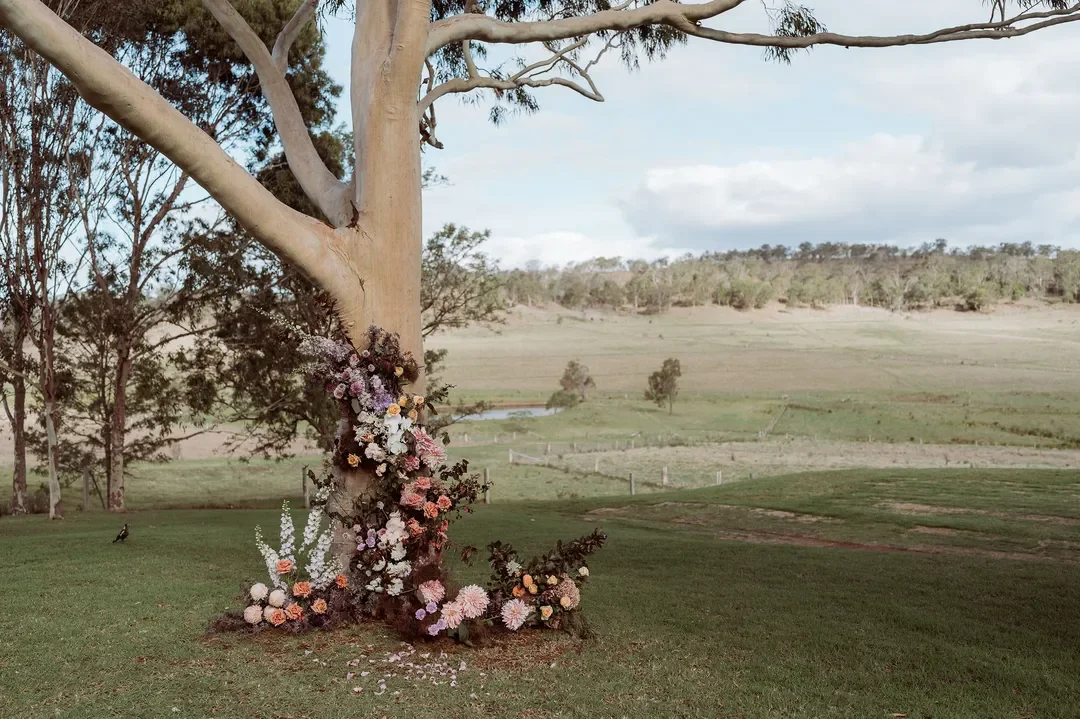 Floral installation climbing the trunk of a gum tree at Annalise and Mitchell’s countryside wedding ceremony.