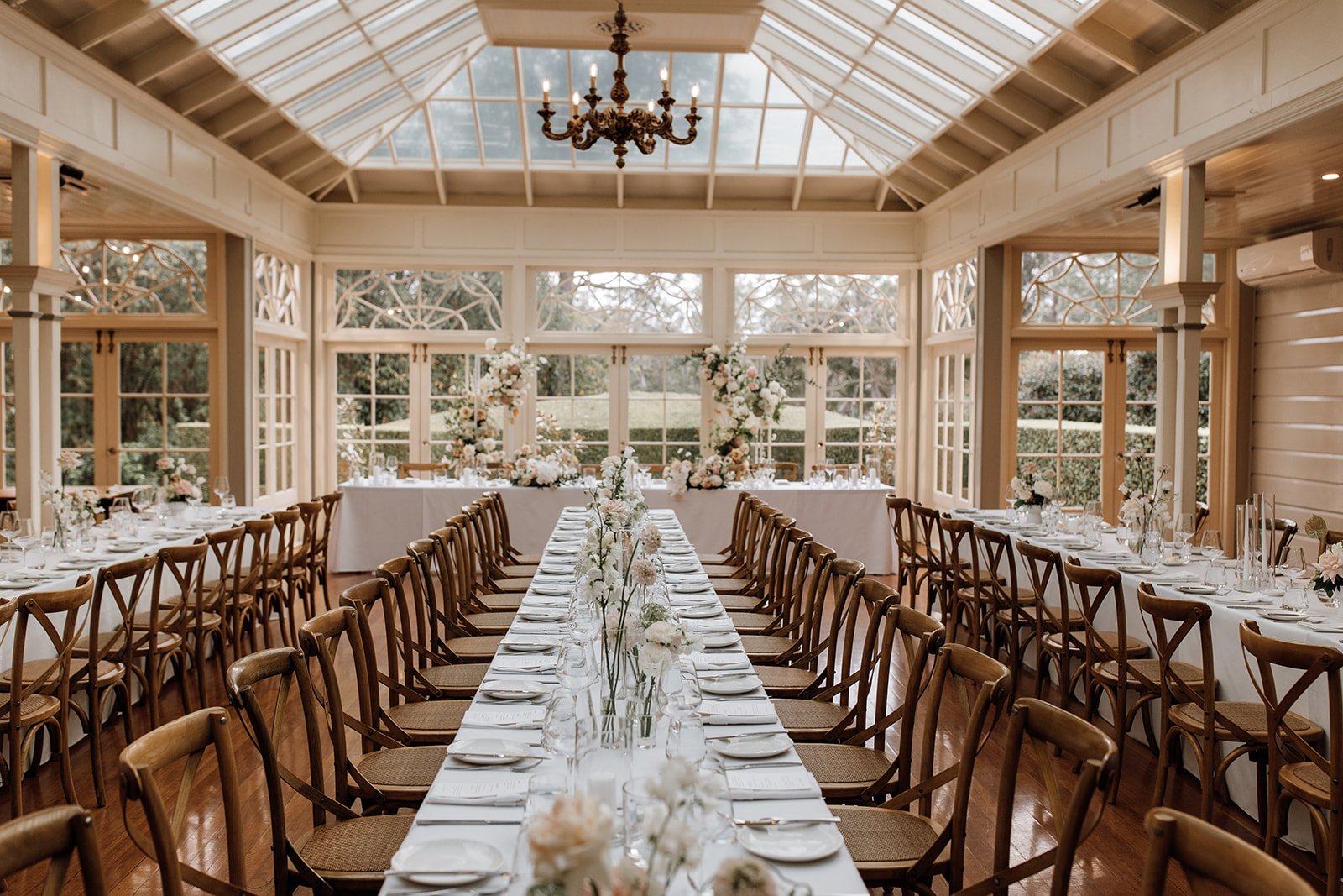 wedding floral reception with floral on long tables and an arbour framing the bridal table with a brass chandelier