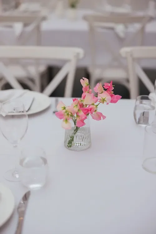Close-up of a simple pink floral bud vase styled on a white wedding reception table