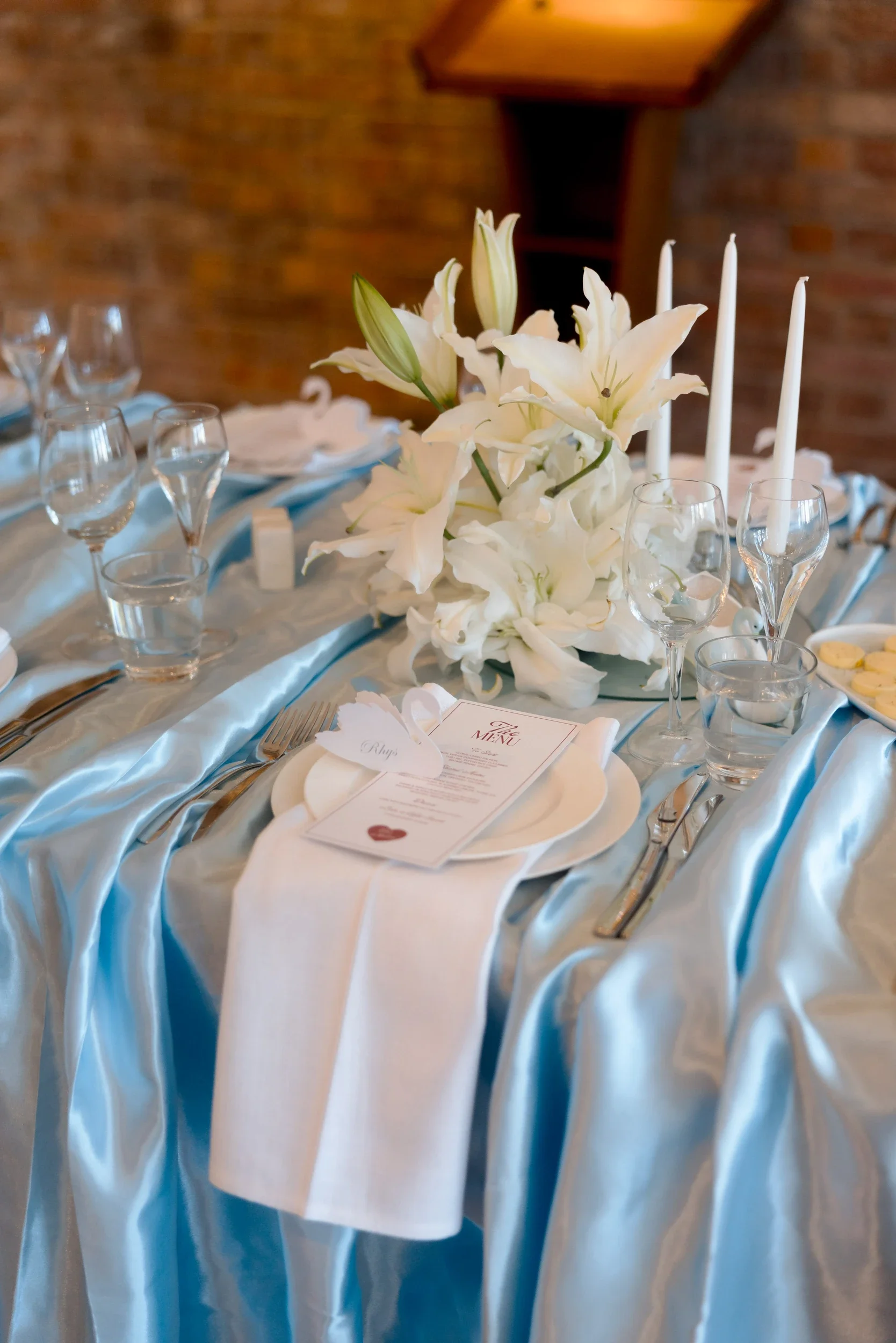 White lily centrepiece and taper candles on a blue satin reception table