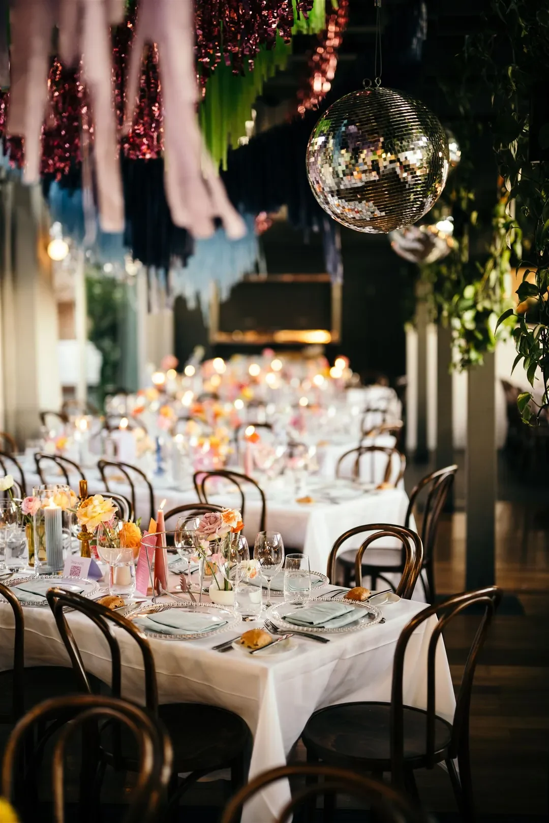 Reception tables decorated with vibrant florals, candles, and a shimmering disco ball hanging overhead at Sarah and Marshall’s wedding.