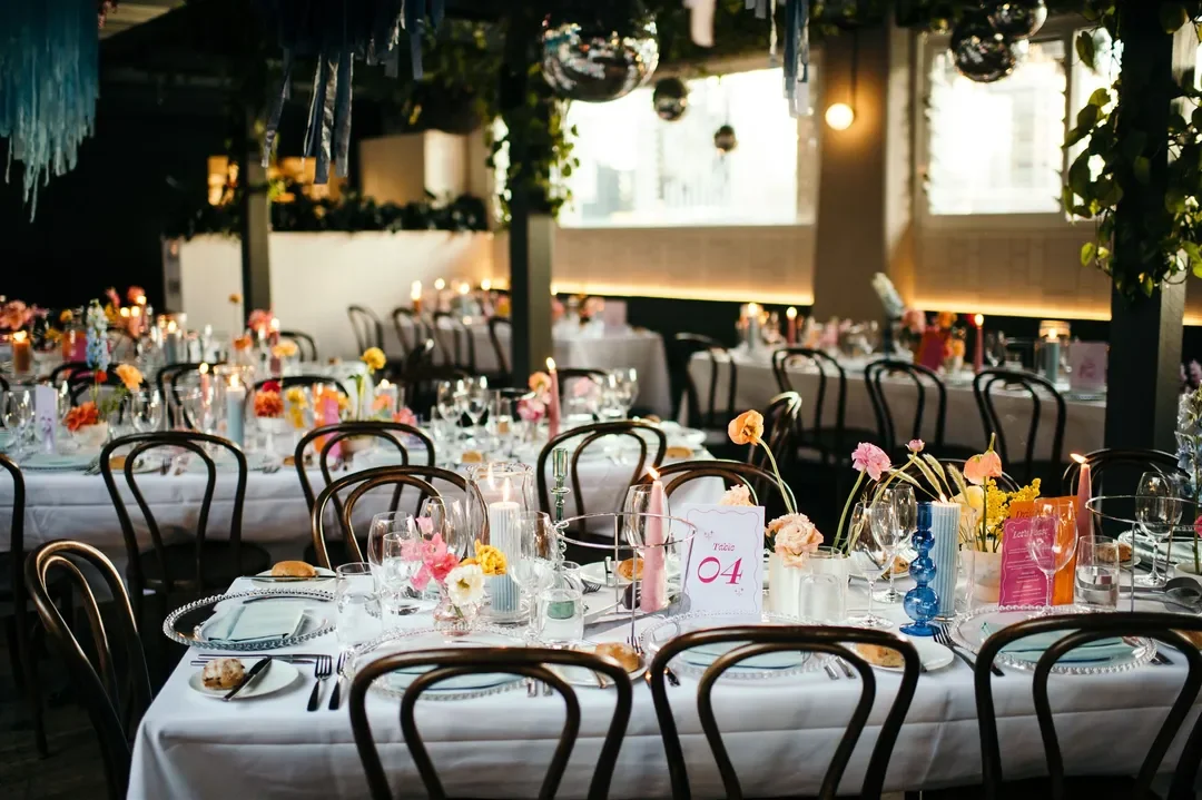 Wide shot of reception tables with pastel florals, candles, and streamers hanging from the ceiling at Sarah and Marshall’s wedding.