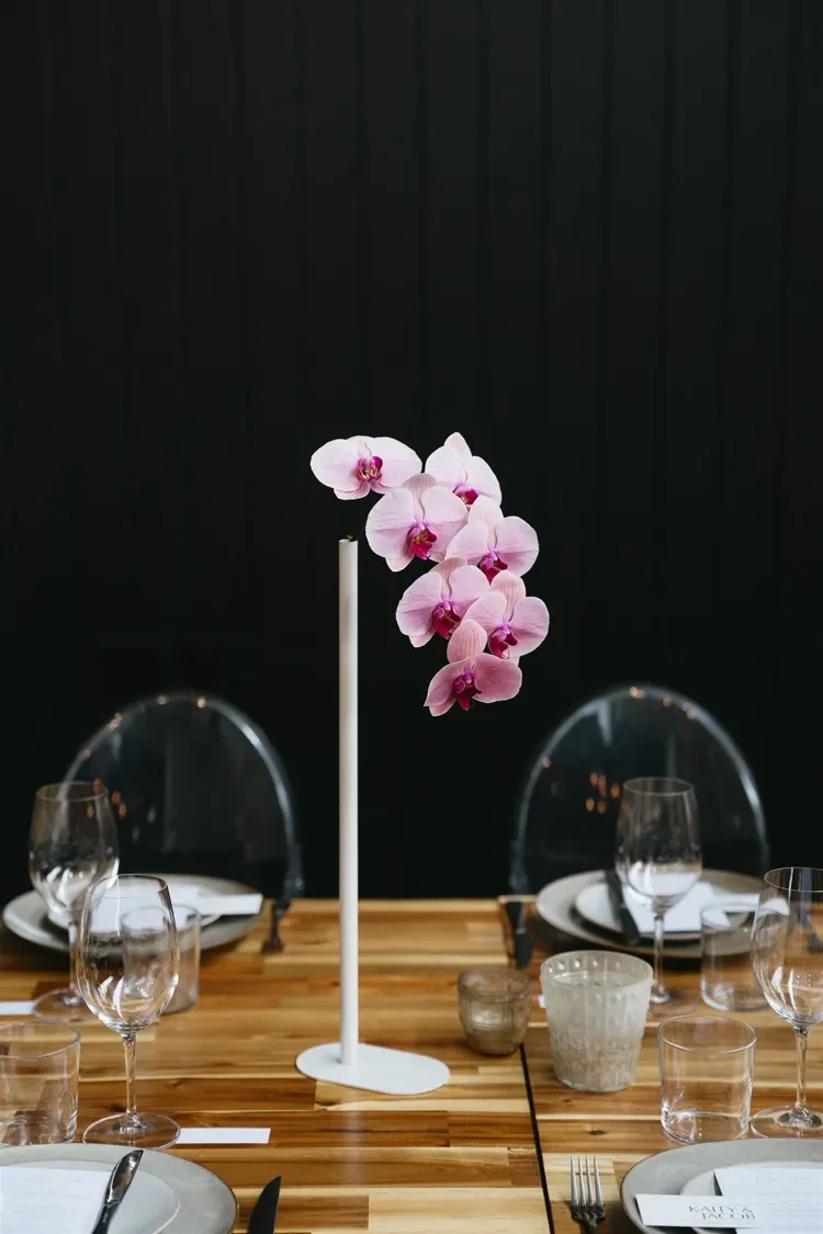 Reception centrepiece featuring a pink orchid stem surrounded by vibrant seasonal blooms in contemporary styling.