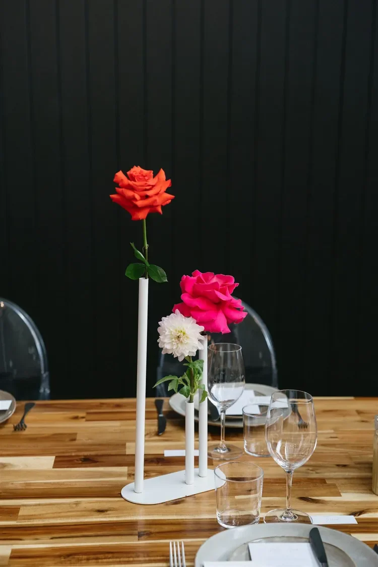 Close-up of wedding reception table décor including glassware, candles and vibrant individual floral stems.