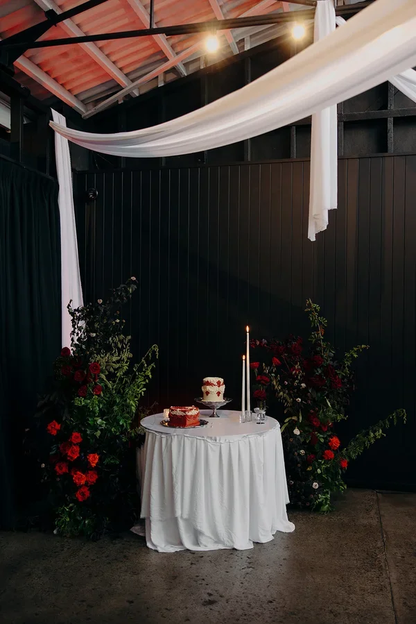Wide view of lush red rose pillars framing the cake table.