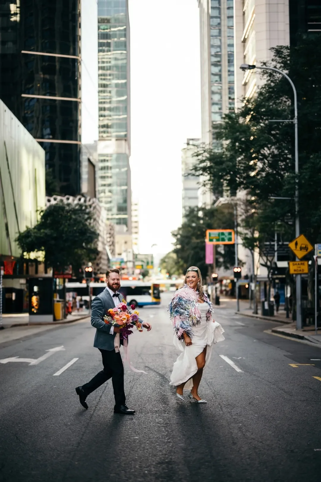 Bride and groom walking through the city streets holding a bright, colourful bouquet at their modern Brisbane wedding.