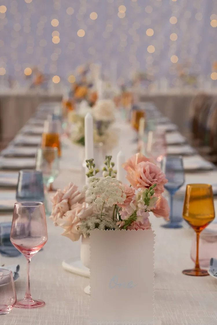 Romantic wedding reception table with pastel florals, candles, and coloured glassware styled under twinkling fairy lights at the Scenic Rim.