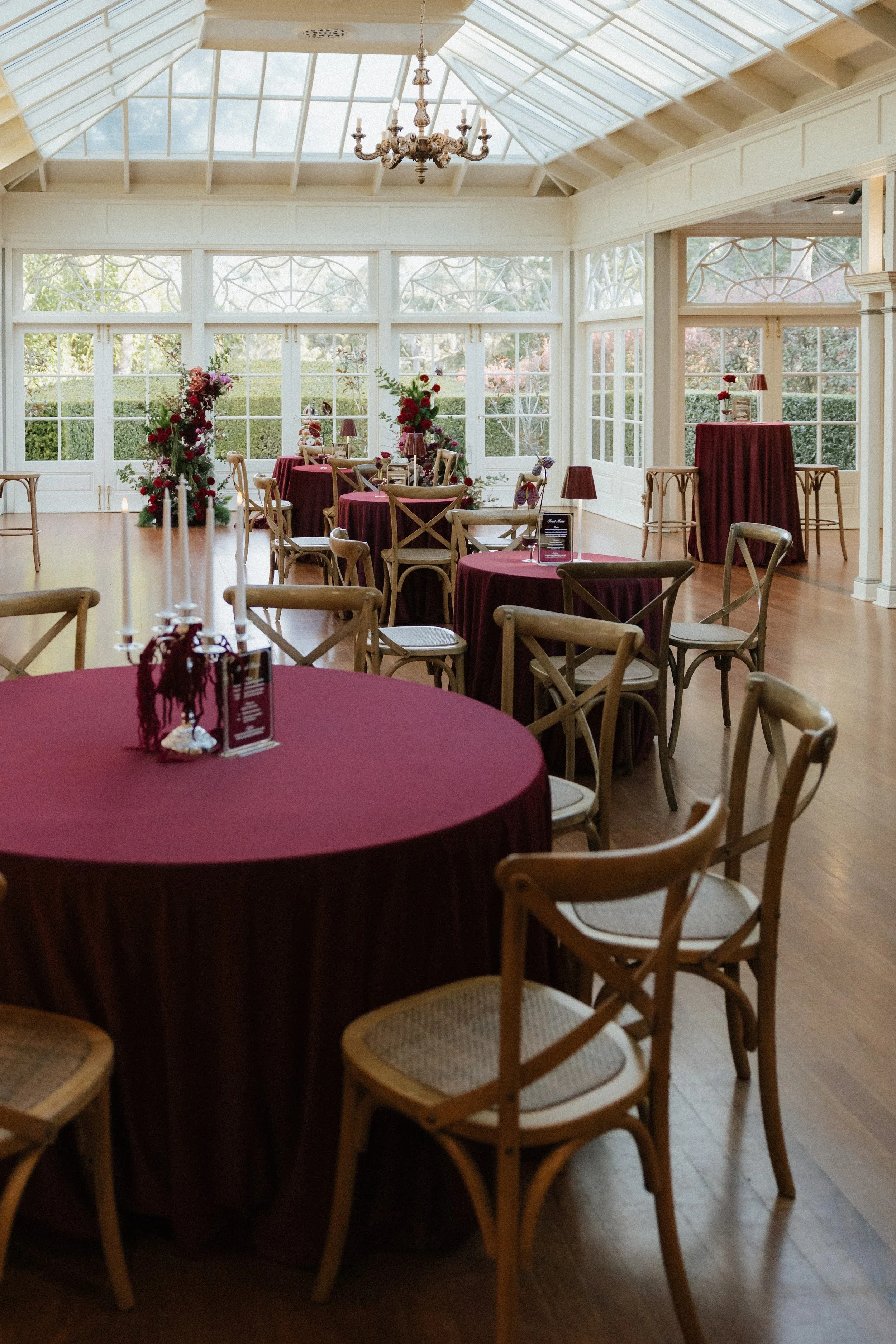 Conservatory reception at Gabbinbar Homestead with round tables dressed in burgundy and deep red floral centrepieces