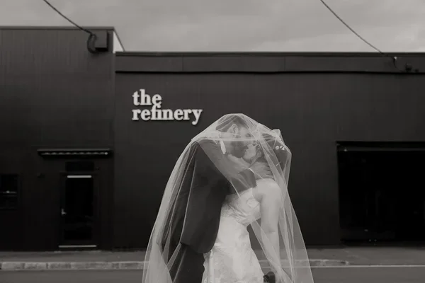 Moody under-veil moment of the bride and groom in front of The Refinery’s dark exterior.