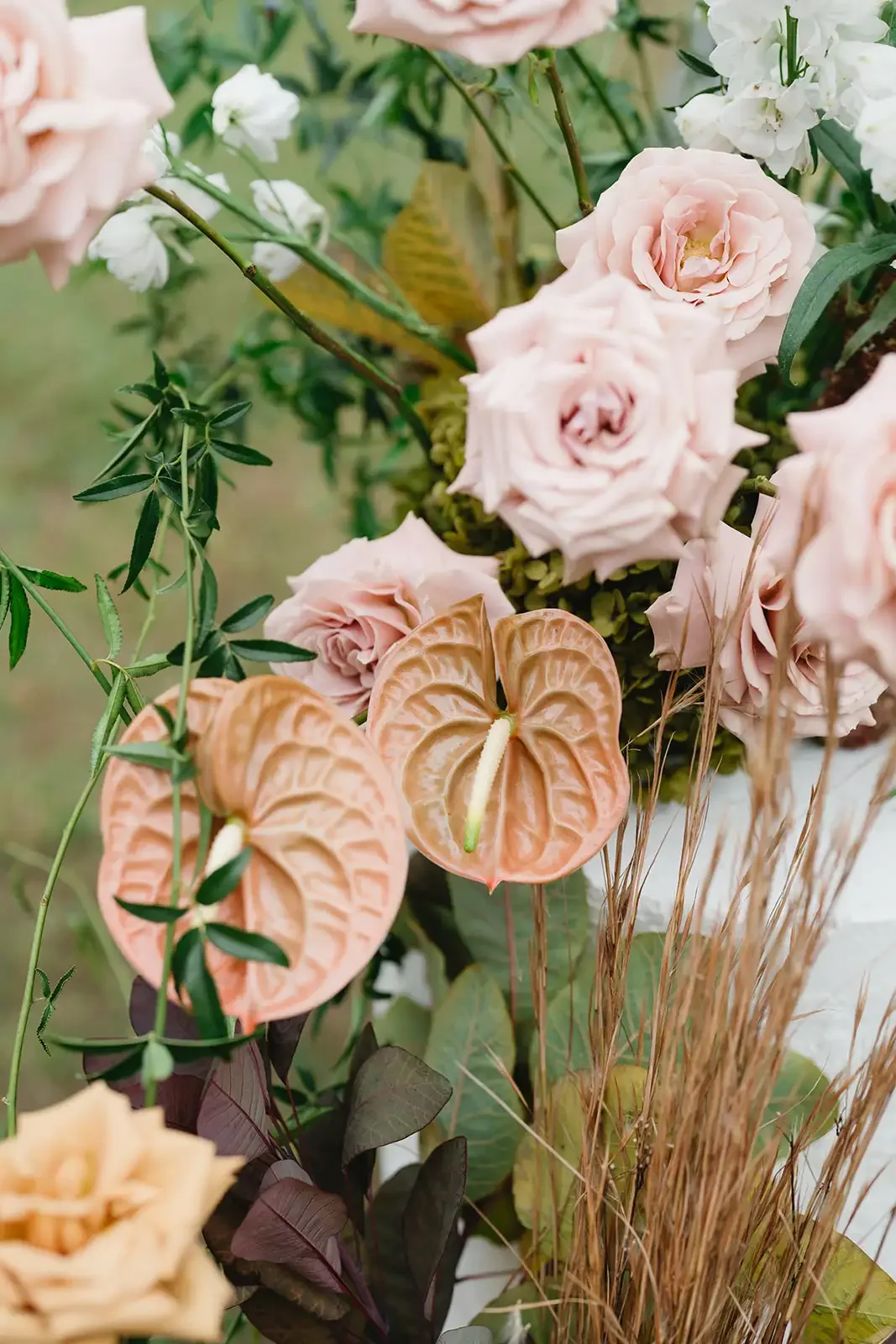 Detail of blush pink roses and peach anthuriums in organic wedding floral arrangements.
