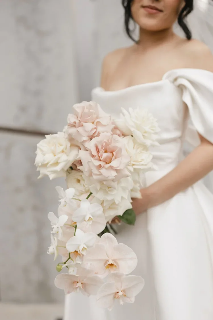 Close-up of the bride’s blush and white rose and orchid bouquet against her modern satin wedding gown.