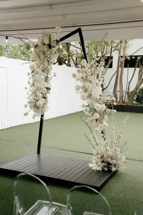 Modern white floral ceremony arch with roses, orchids and seasonal blooms at The Refinery Brisbane wedding by Garden Graffiti