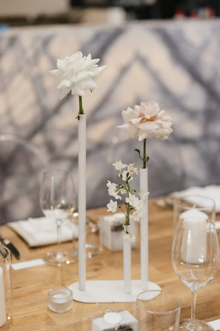 Minimalist tabletop arrangement featuring white and blush single-stem flowers in modern white bud vases.