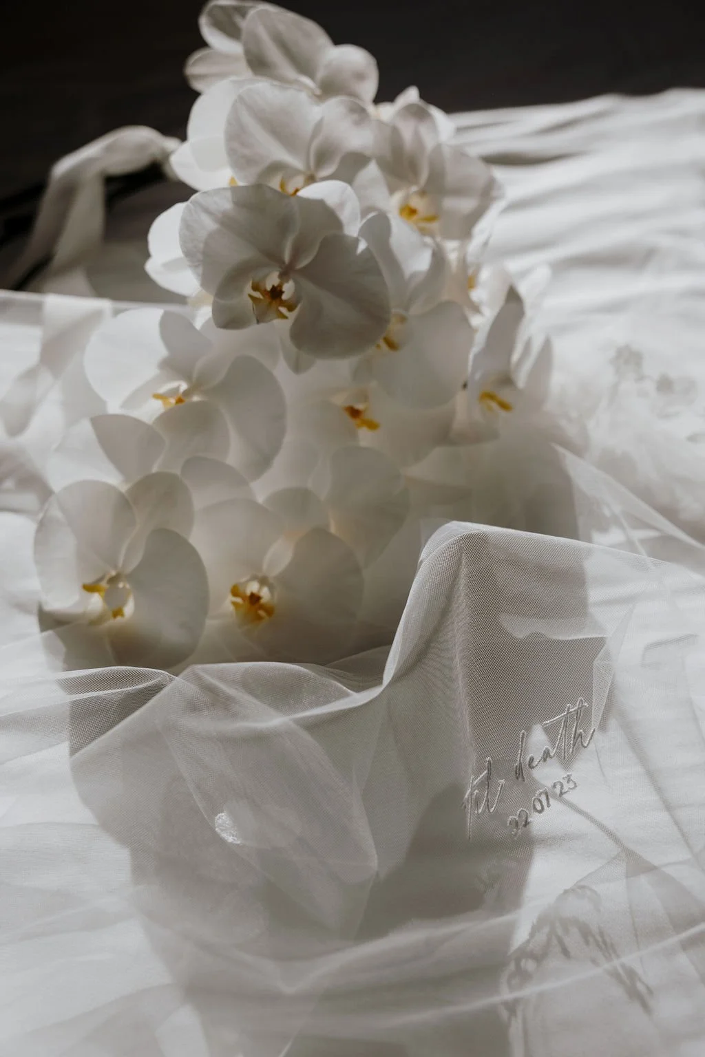 Close-up of cascading white phalaenopsis orchids resting on the bride’s embroidered wedding veil.