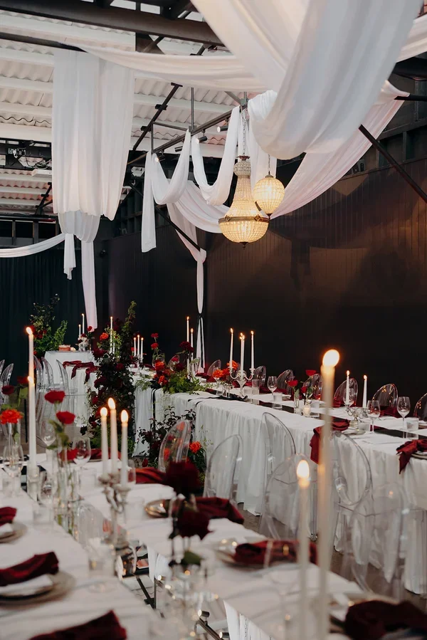 Dramatic reception styling with white drapery from ceiling and red floral accents, candelight and red velvet napkins.