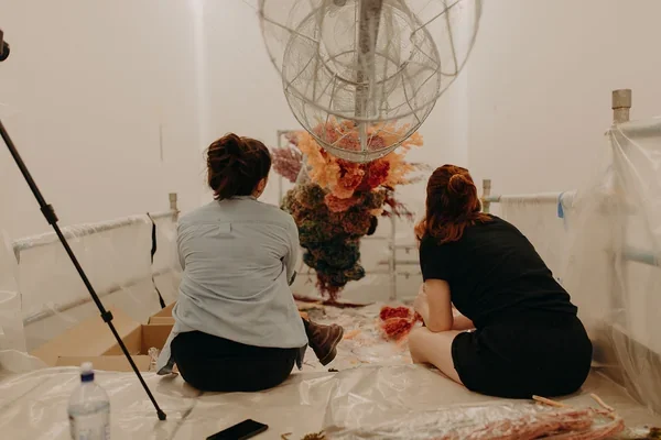 Two Garden Graffiti florists sitting beneath the installation structure while building the large-scale floral artwork at West Village.