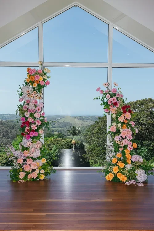 Colourful Garden Graffiti ceremony pillars filled with pink, peach, and seasonal blooms overlooking a scenic landscape